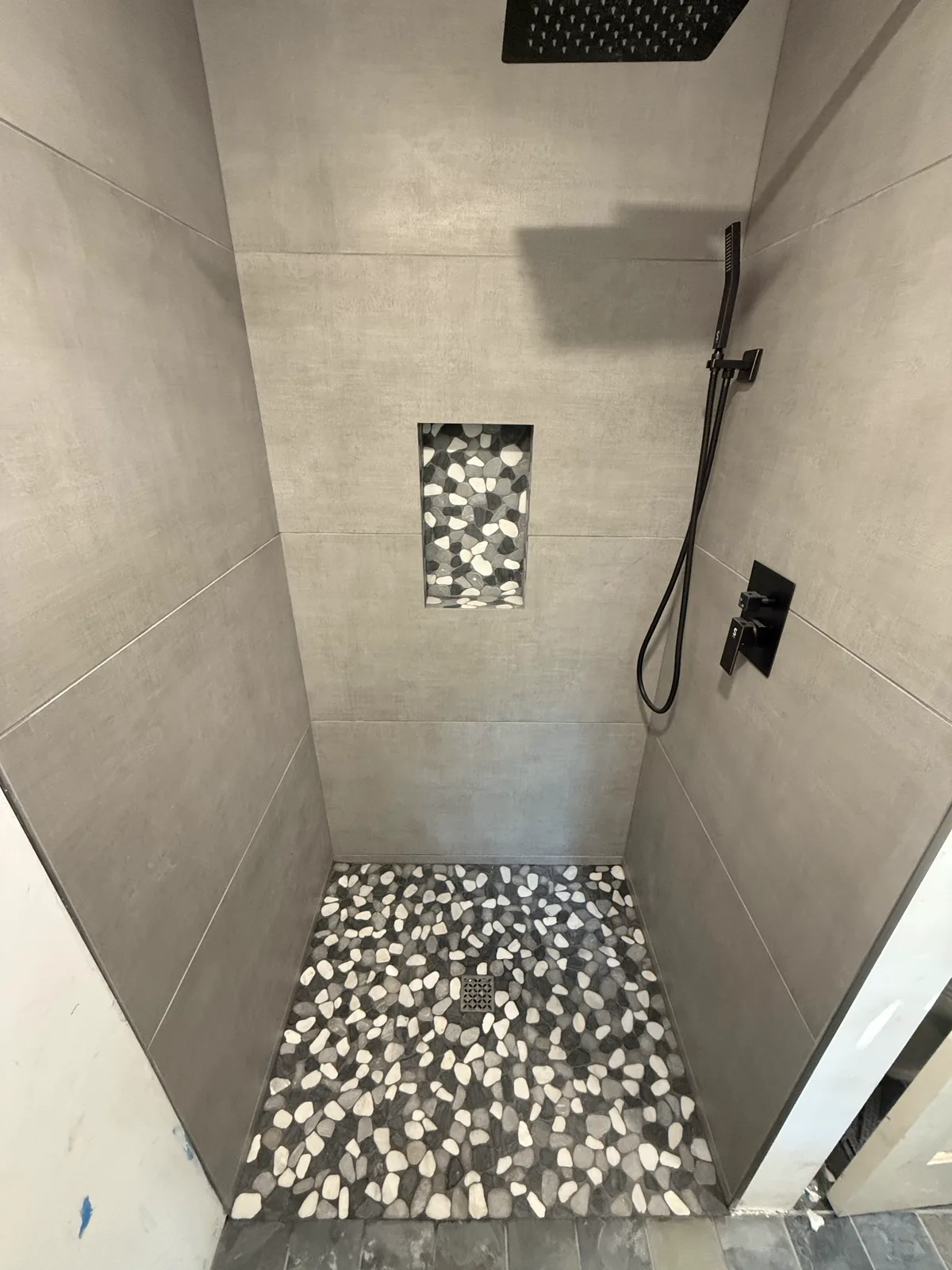 Custom tiled shower with large-format gray tile, mosaic niche, and pebble floor